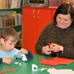 Bibliotekarka pokazująca chłopcu jak tworzyć papierowy kotylion